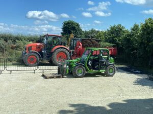 Picture of a red tractor and trailer parked next to a green tele handler.