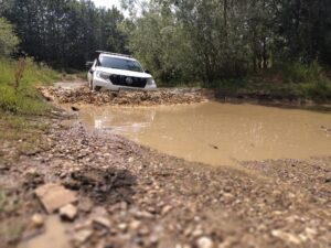 A white off Road vehicle wading through muddy water.